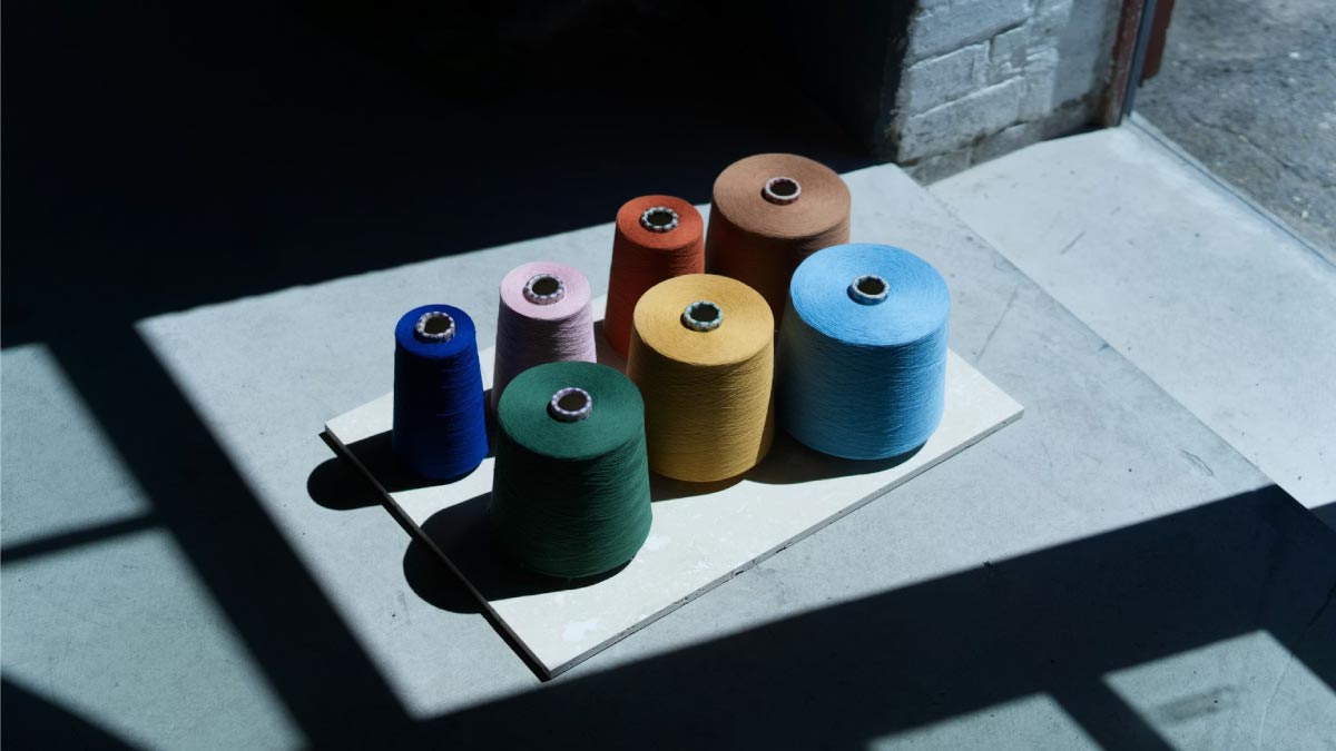 Spools of colorful textile yarn in shades of blue, yellow, green, and pink, representing raw material selection in apparel sourcing.