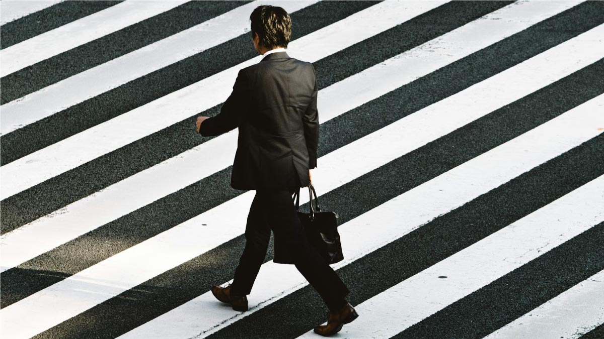 A businessman in a suit crossing a black and white striped crosswalk, symbolizing the journey toward ethical apparel sourcing for global brands.